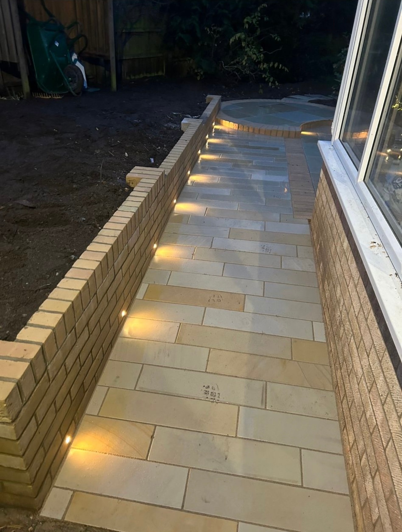 Patio pathway with recessed brick wall lights on sandstone paving at night