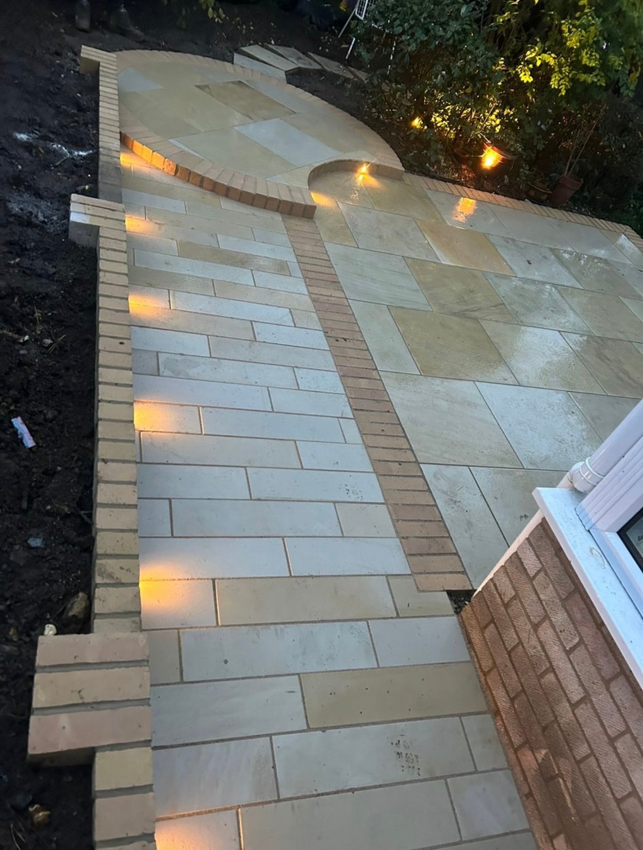 Wide view of curved patio with recessed brick wall lights and sandstone paving