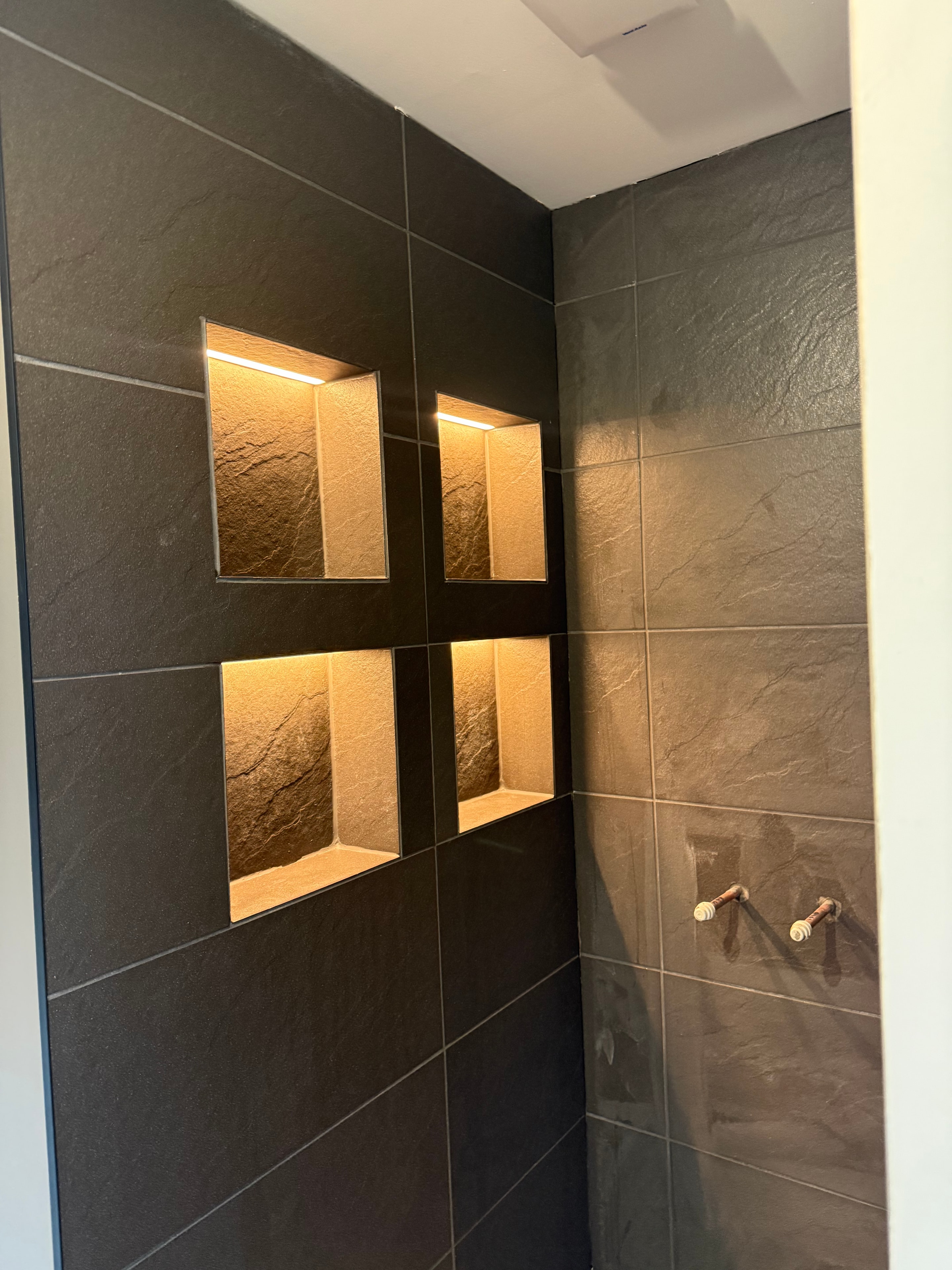 Illuminated recessed niches in dark tiled bathroom